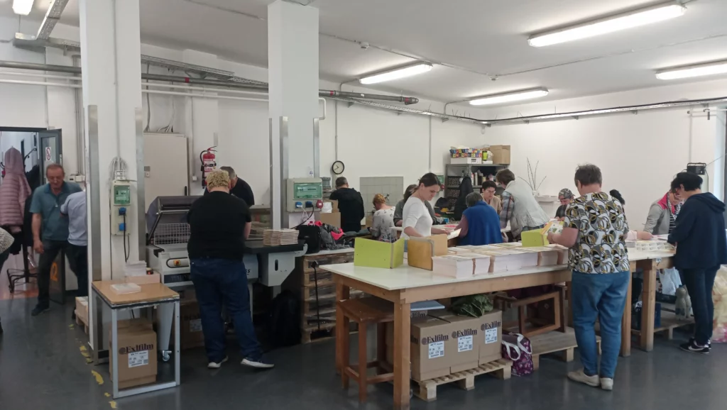 A dolgozók a papíráruk hajtogatását, ragasztását végzik a kötészeti üzemben.