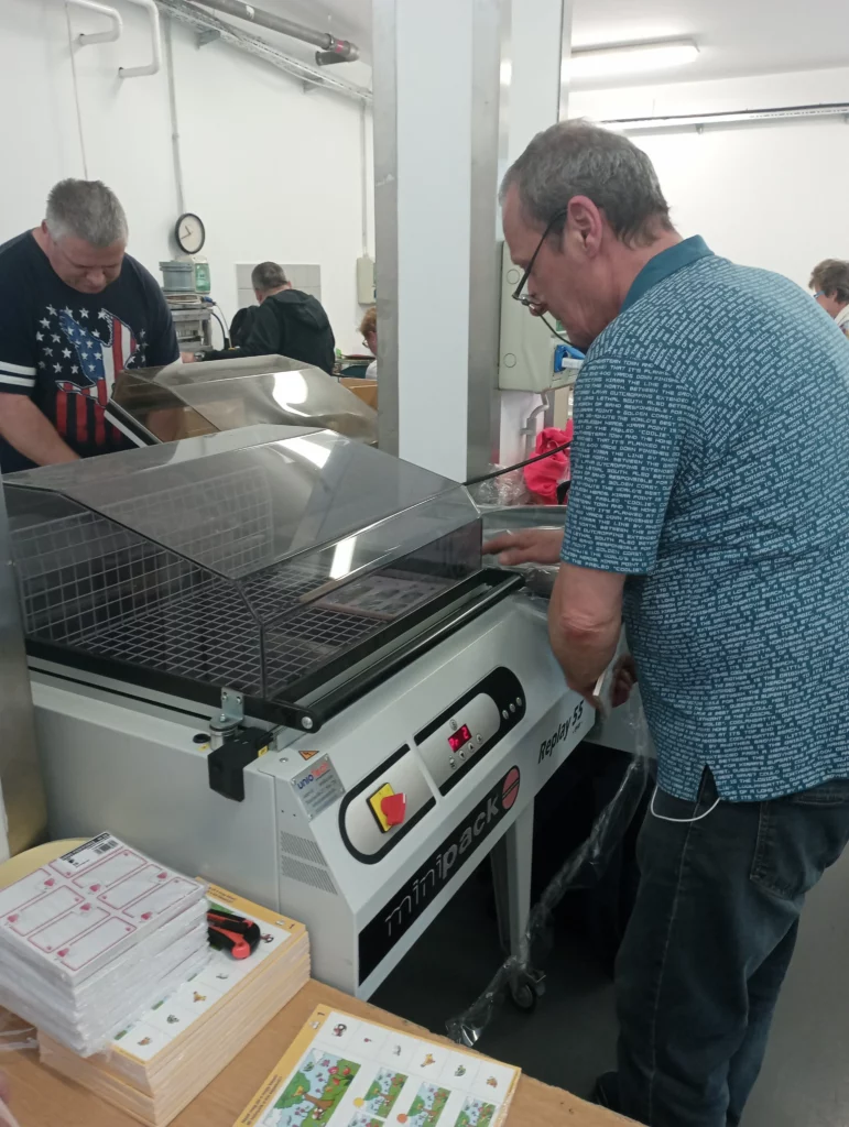 Fóliázó gépet kezelő dolgozók. A zsugorfóliázási eljárás által a termékek esztétikus csomagolást kapnak.