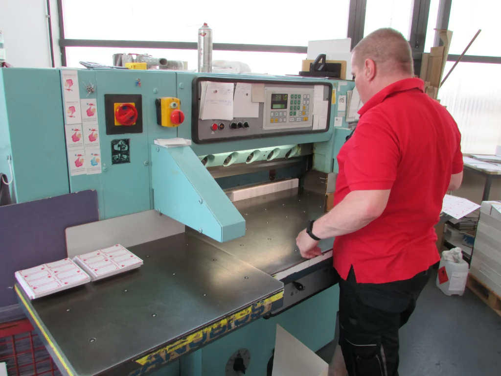 Betanított munkás a papírvágó gép segítségével precízen méretre darabolja a papírárut.